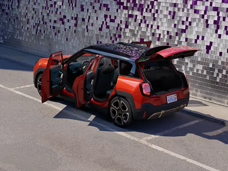Gatvėje stovinčio raudonos Rebel Red  spalvos visiškai elektrinio MINI Aceman galinis vaizdas iš viršaus su juodos spalvos stogu ir atviromis durelėmis.