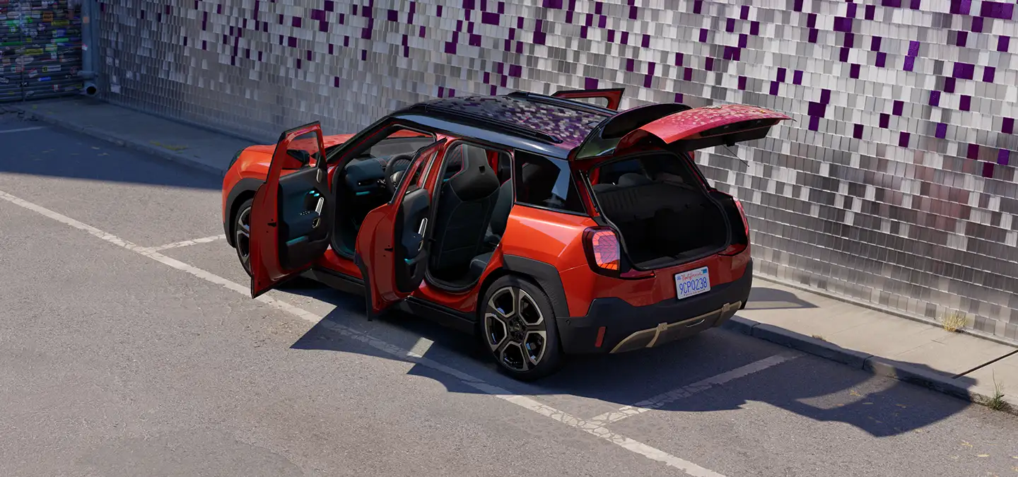 Gatvėje stovinčio raudonos Rebel Red  spalvos visiškai elektrinio MINI Aceman galinis vaizdas iš viršaus su juodos spalvos stogu ir atviromis durelėmis.