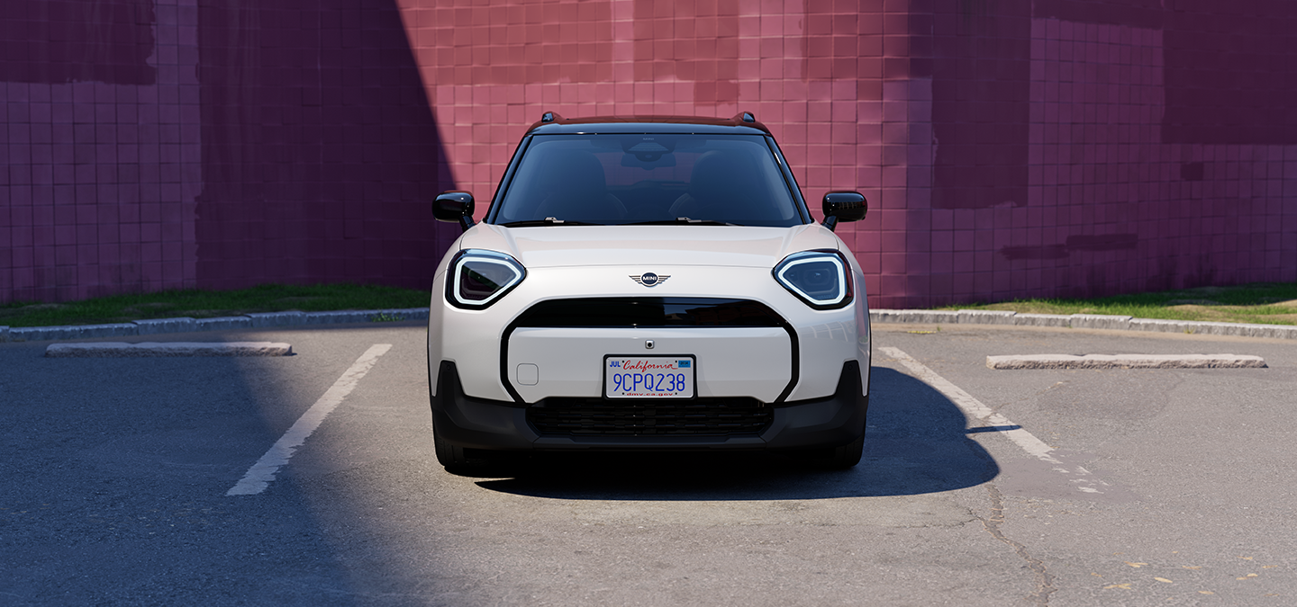 Parkinge stovinčio baltos Nanuq White spalvos visiškai elektrinio  MINI Aceman vaizdas iš priekio su juodos spalvos stogu.