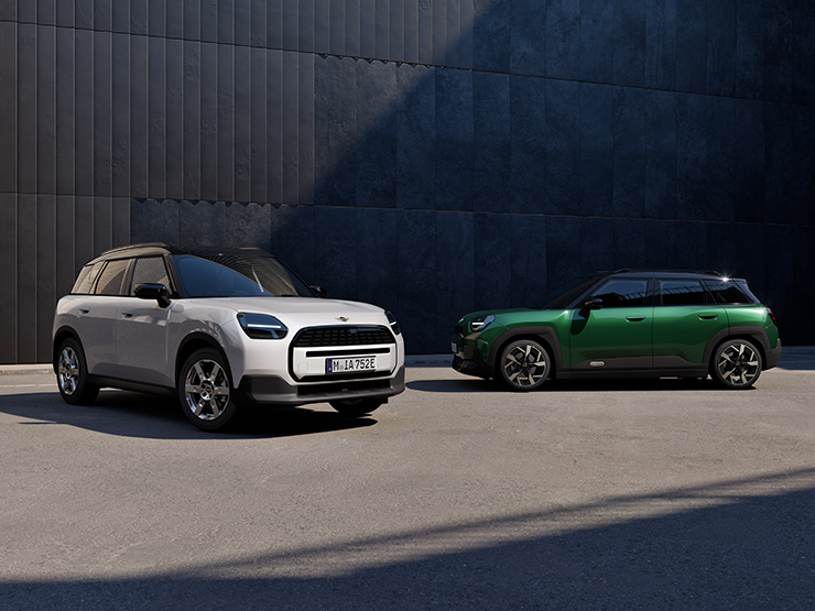 Gatvėje stovinčio baltos Nanuq White spalvos visiškai elektrinio MINI Aceman priekinis vaizdas iš šono su žalios British Racing Green ir juodos spalvos stogu.