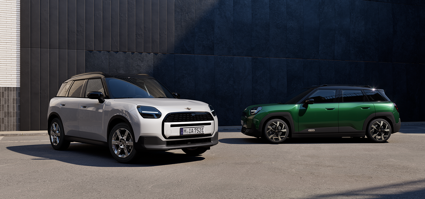 Gatvėje stovinčio baltos Nanuq White spalvos visiškai elektrinio MINI Aceman priekinis vaizdas iš šono su žalios British Racing Green ir juodos spalvos stogu.
