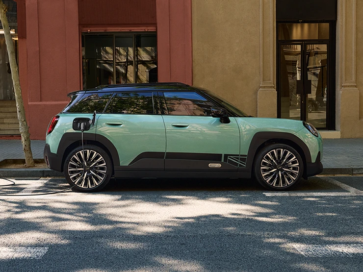 Gatvėje stovinčio žalsvos Ocean Wave Green spalvos visiškai elektrinio MINI Aceman vaizdas iš šono su juodos spalvos stogu.