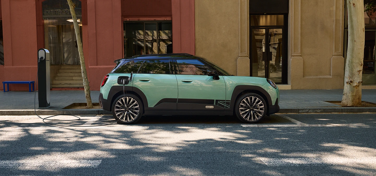 Gatvėje stovinčio žalsvos Ocean Wave Green spalvos visiškai elektrinio MINI Aceman vaizdas iš šono su juodos spalvos stogu.