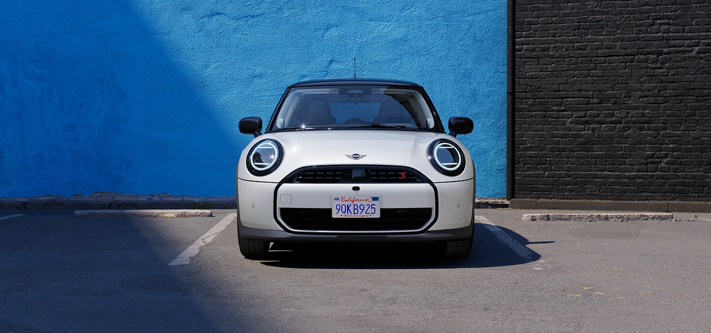 Parkinge stovinčio baltos Nanuq White spalvos MINI Cooper vaizdas iš priekio su juodu stogu.