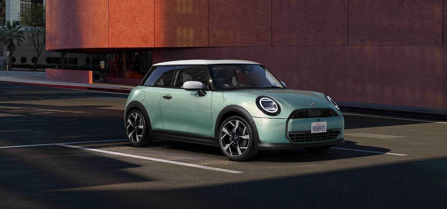 Žalios Ocean Wave Green spalvos MINI Cooper vaizdas iš priekinio šono su baltu stogu.