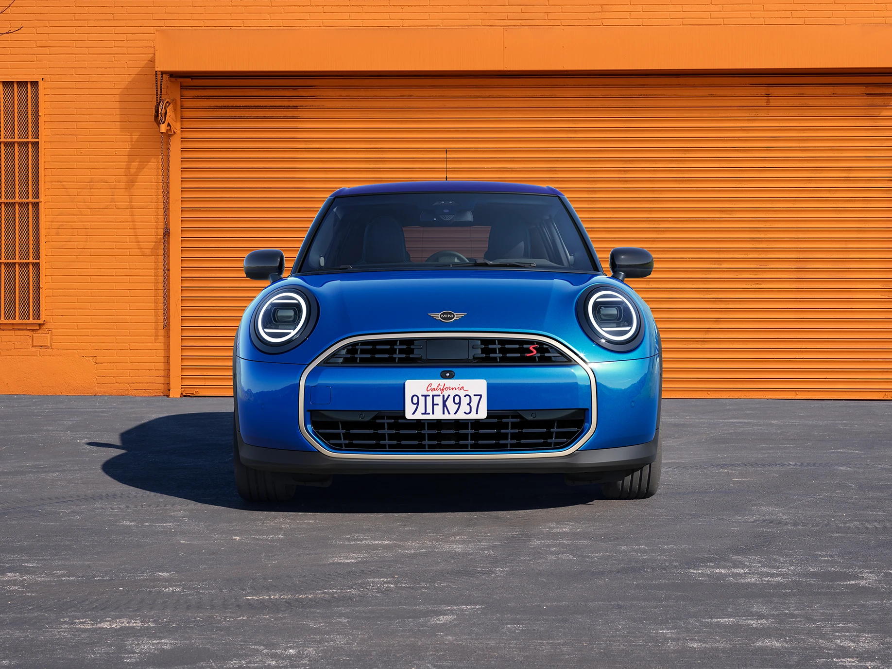 Mėlynos Icy Sunshine Blue spalvos MINI Cooper 5-durio vaizdas iš priekio su daugiatoniu mėlynu stogu.