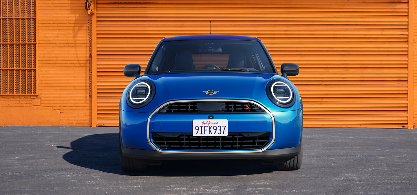 Mėlynos Icy Sunshine Blue spalvos MINI Cooper 5-durio vaizdas iš priekio su daugiatoniu mėlynu stogu.