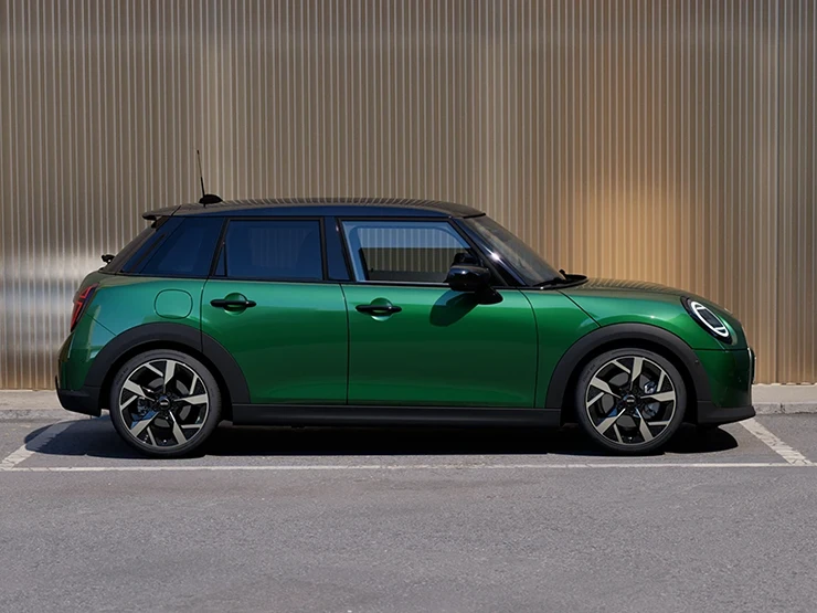 Parkinge stovinčio British Racing Green žalios spalvos MINI Cooper 5-durio vaizdas iš šono su juodos spalvos stogu.