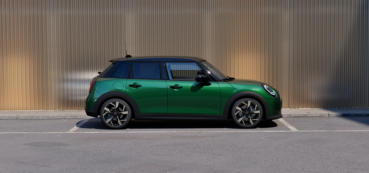 Parkinge stovinčio British Racing Green žalios spalvos MINI Cooper 5-durio vaizdas iš šono su juodos spalvos stogu.