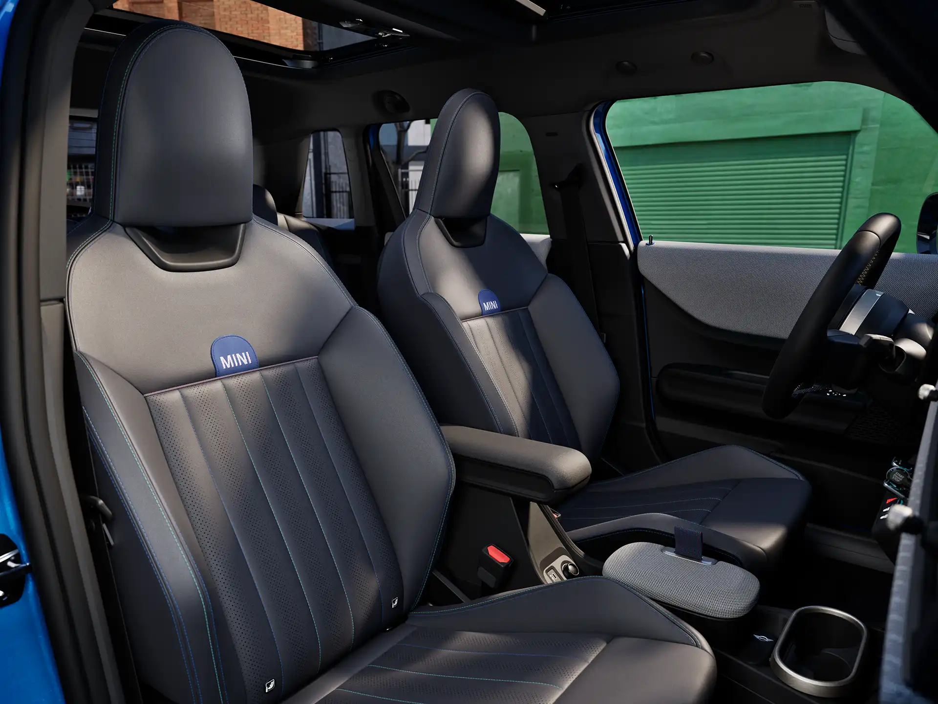 MINI Cooper 5-durio interjeras su prietaisų skydeliu, vairu, apvaliu ekranu, panoraminiu stikliniu stoglangiu ir priekinių sėdynių atlošais.