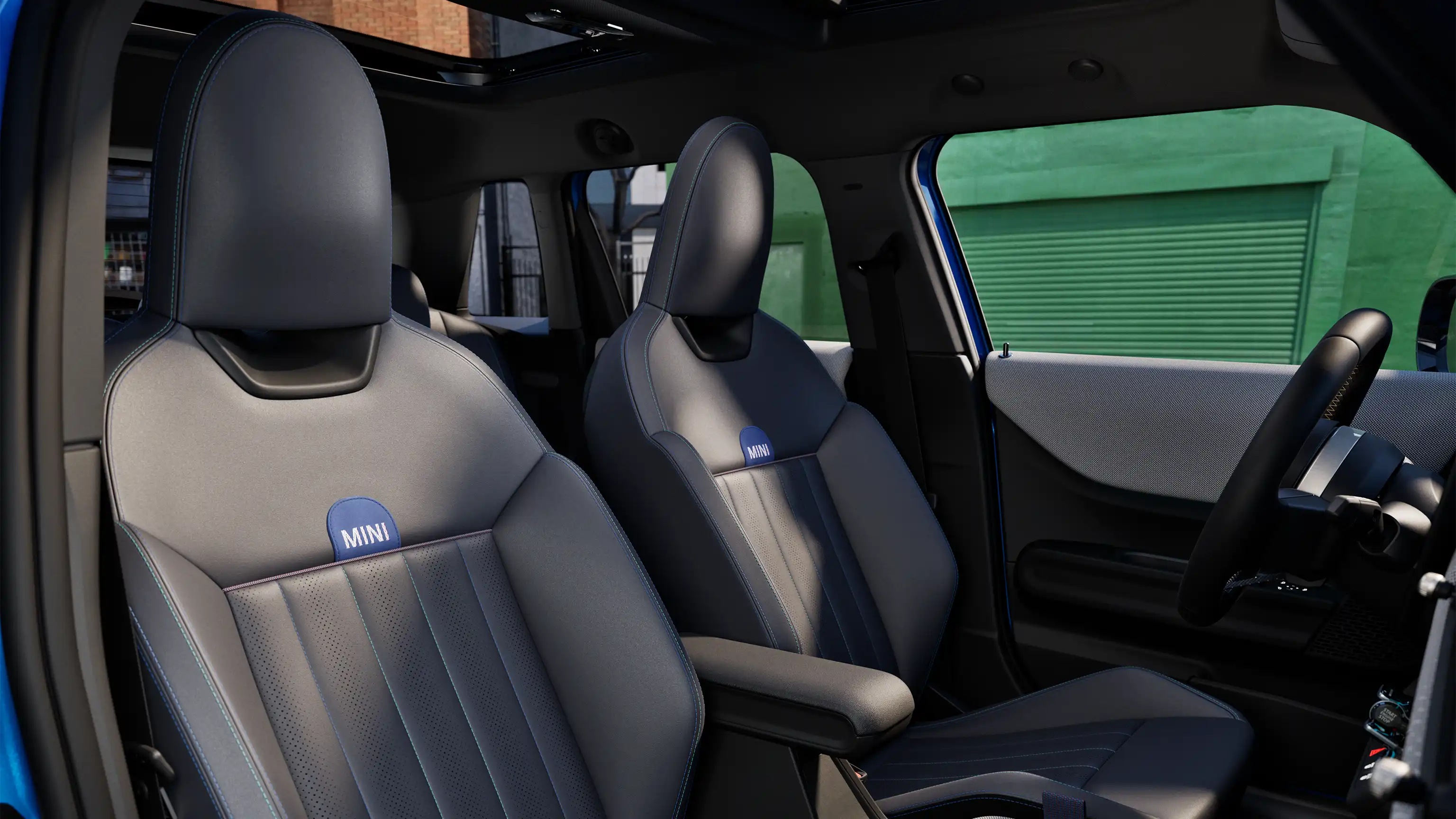 MINI Cooper 5-durio interjeras su prietaisų skydeliu, vairu, apvaliu ekranu, panoraminiu stikliniu stoglangiu ir priekinių sėdynių atlošais.