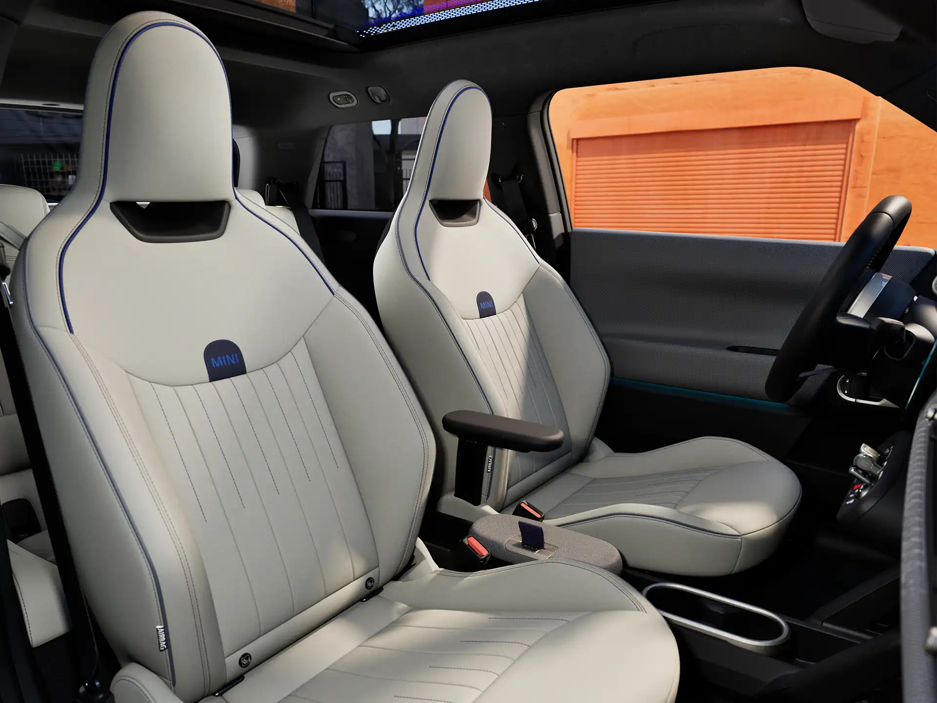 Visiškai elektrinio MINI Cooper interjero vaizdas su prietaisų skydeliu, vairu, apvaliu ekranu, panoraminiu stoglangiu ir priekinių sėdynių atlošais