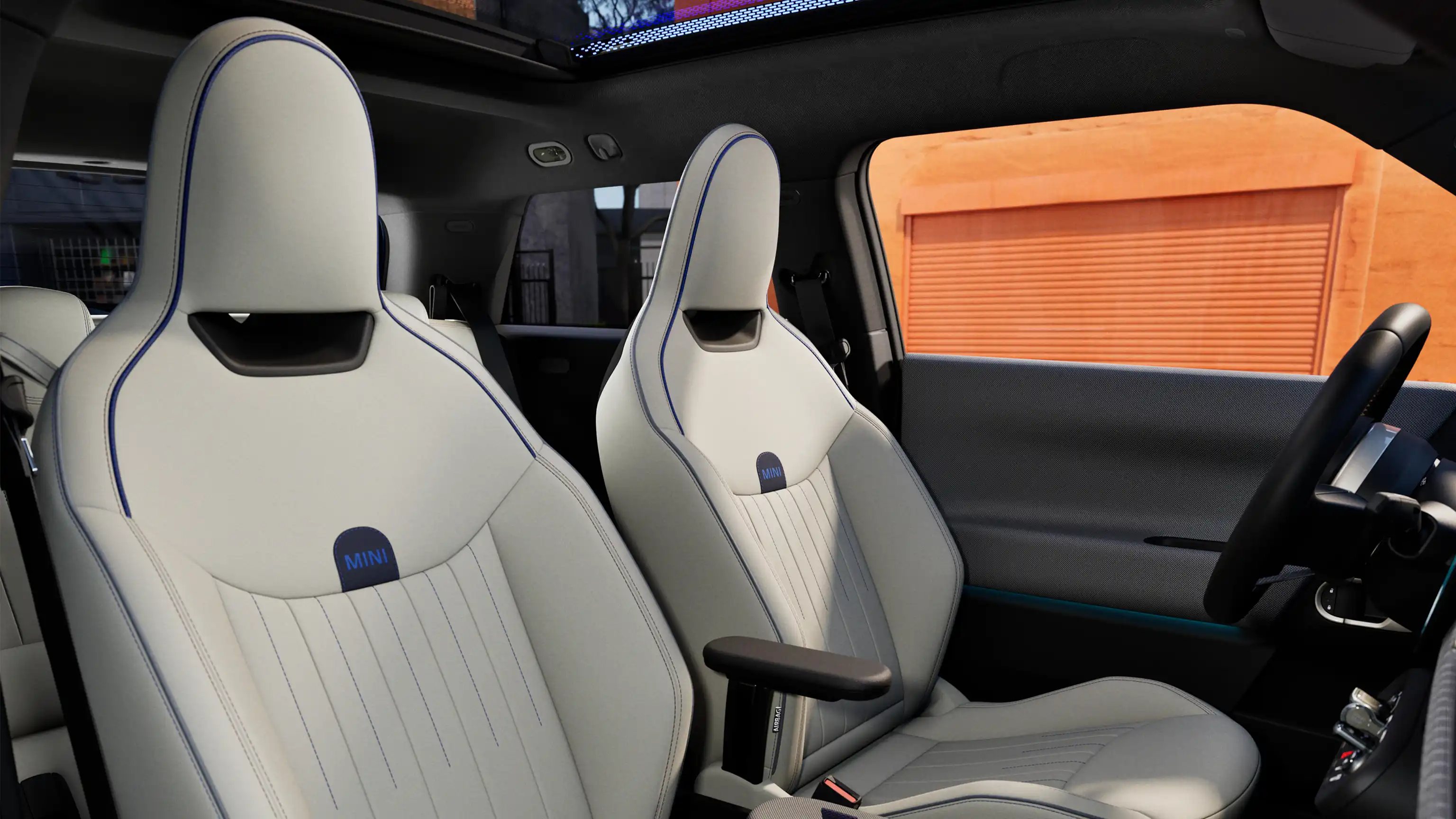 Visiškai elektrinio MINI Cooper interjero vaizdas su prietaisų skydeliu, vairu, apvaliu ekranu, panoraminiu stoglangiu ir priekinių sėdynių atlošais