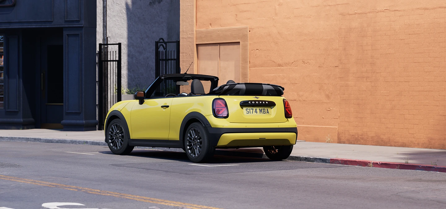 Parkinge stovinčio MINI Cooper kabrioleto  geltonos Sunnyside Yellow spalvos galinis vaizdas iš kairės.