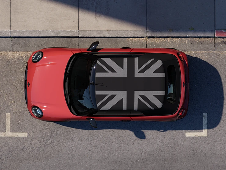 Gatvėje stovinčio pilkos Copper Grey spalvos MINI Cooper kabrioleto su MINI Yours stogu vaizdas iš viršaus