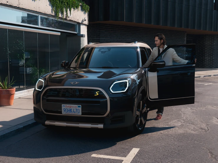 Midnight Black juodos spalvos visiškai elektrinio MINI Countryman gatvėje vaizdas iš priekio su pilkos spalvos Vibrant Silver stogu.