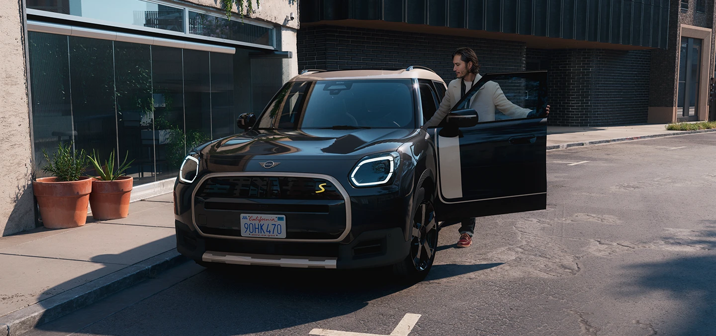 Midnight Black juodos spalvos visiškai elektrinio MINI Countryman gatvėje vaizdas iš priekio su pilkos spalvos Vibrant Silver stogu.