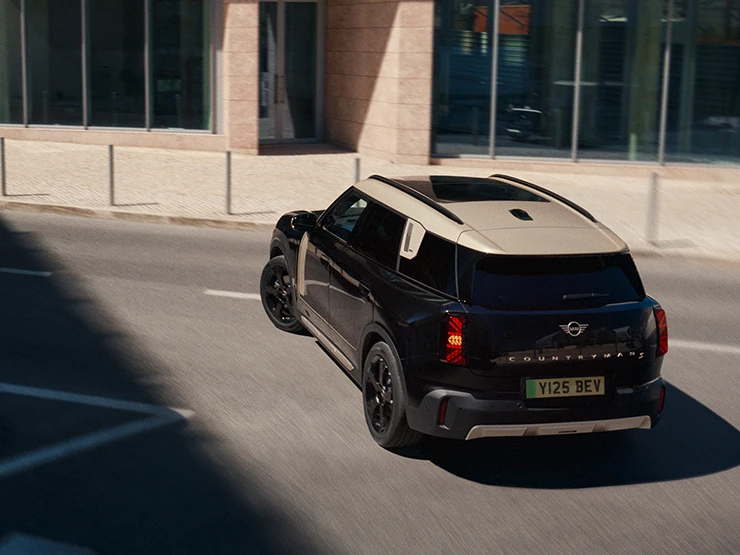 Juodos Midnight Black spalvos visiškai elektrinio MINI Countryman galinis vaizdas iš viršaus parkinge su pilkos spalvos Vibrant Silver stogu.
