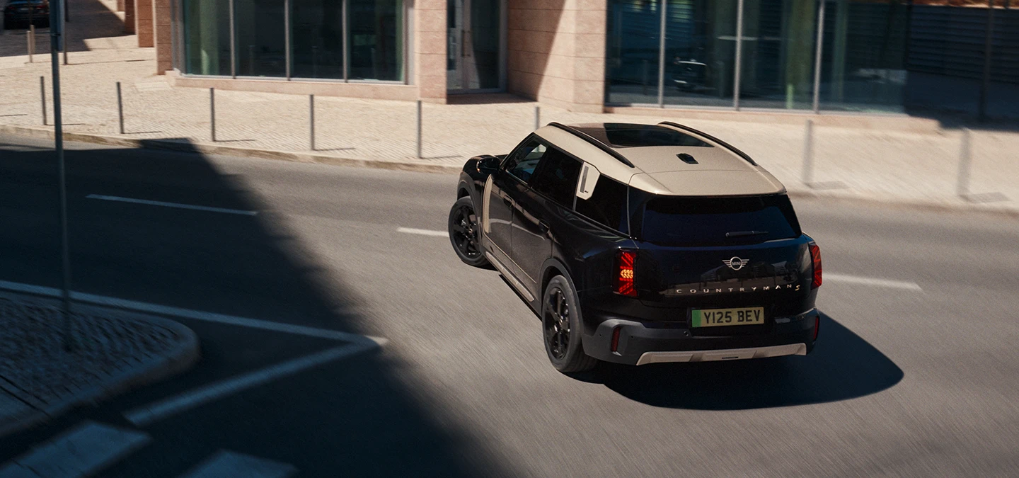 Juodos Midnight Black spalvos visiškai elektrinio MINI Countryman galinis vaizdas iš viršaus parkinge su pilkos spalvos Vibrant Silver stogu.