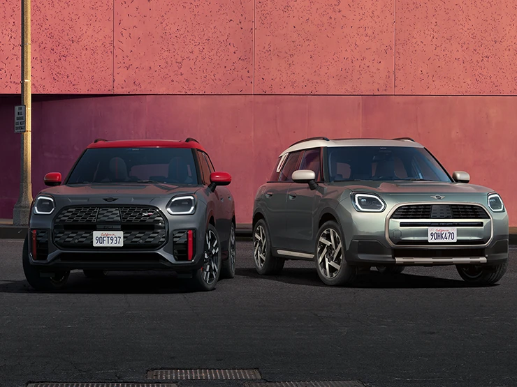 Vienas šalia kito stovinčių MINI Countryman JCW pilkos Legend Grey su raudonos spalvos stogu ir MINI Countryman žalios Smokey Green su pilkos Vibrant Silver spalvos vaizdas iš priekio