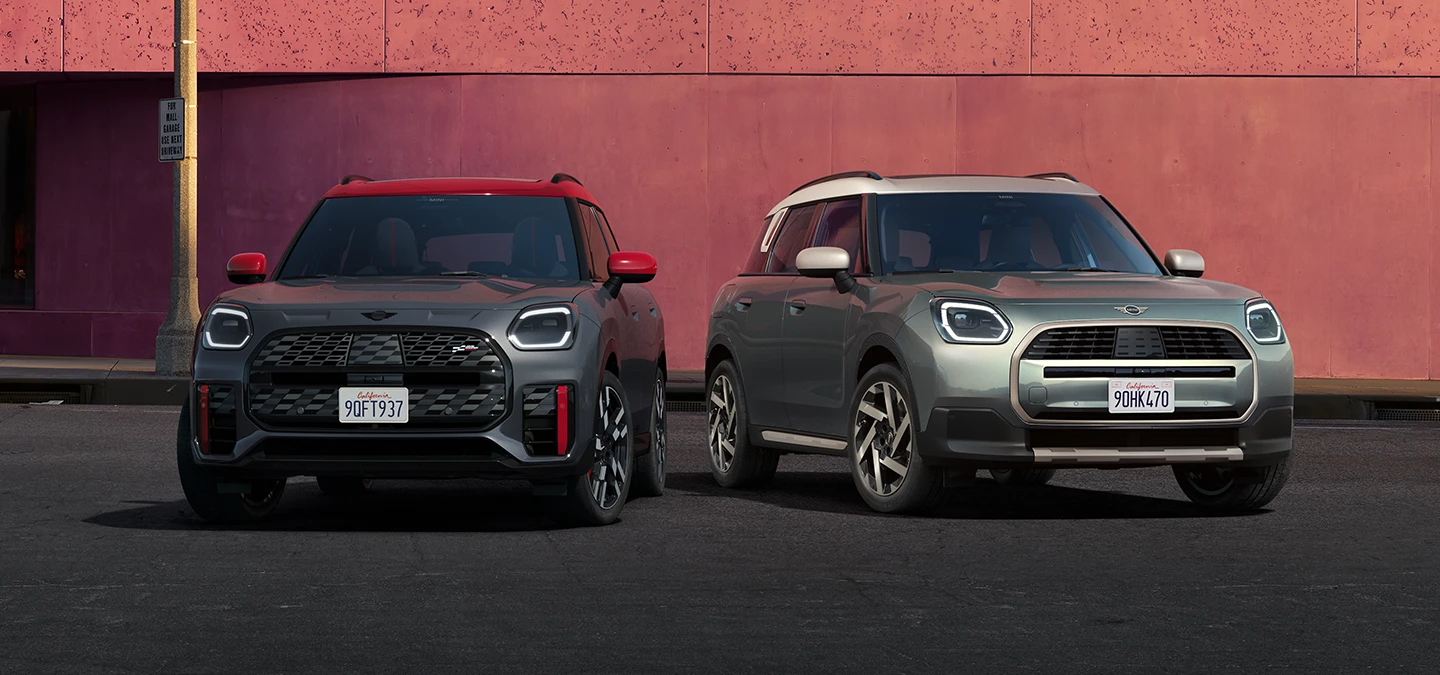 Vienas šalia kito stovinčių MINI Countryman JCW pilkos Legend Grey su raudonos spalvos stogu ir MINI Countryman žalios Smokey Green su pilkos Vibrant Silver spalvos vaizdas iš priekio