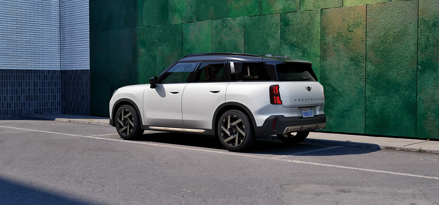 Gatvėje stovintis MINI Countryman baltos Nanuq White spalvos su juoda stogo bagažine.