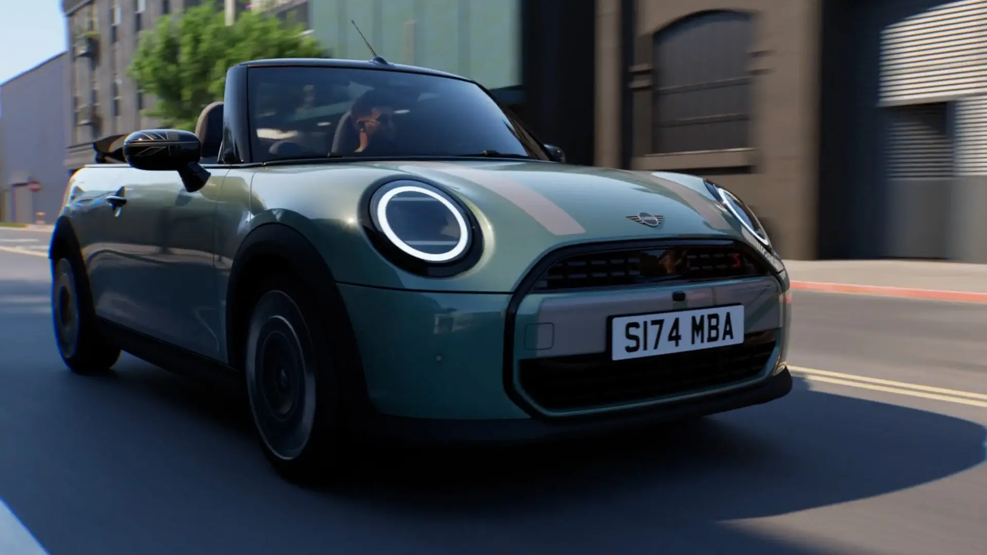 Mieste važiuojantis žalios Ocean Wave Green spalvos MINI kabrioletas su MINI Heritage baltais lipdukais ir Union Jack veidrodėlių korpusais.